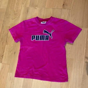 Rosa t-shirt från Puma - Säljer en rosa t-shirt från Puma med logga och text framtill. 