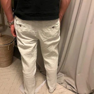 Vita linnebyxor med knytskärp från Lindbergh - Säljer ett par vita linnebyxor med knytskärp i midjan. Byxorna har normal passform, raka ben och fickor både fram och bak. Perfekta för en avslappnad och stilren look.