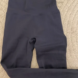 Svarta ribbade tights från Stronger - Säljer ett par svarta ribbade tights från Stronger. De har hög midja och är i ett stretchigt material. Dem har väldigt små noppror på knäna men ingenting man ser. Går säkert bort med noppar borste/ maskin