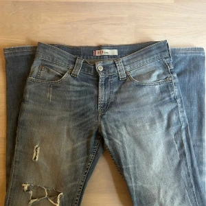  Levis 511 Slim - Säljer ett par blå jeansbyxor från 511 Slim med slitningar och hål på ena benet. Jeansen har klassisk femficksdesign, normalhög midja och smal passform. Perfekta för en avslappnad och trendig look. Bara höra av sig vid eventuella funderingar!