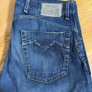 Blå jeansbyxor från Replay - Säljer ett par klassiska blå jeans från Replay med raka ben och snygga slitningar. Byxorna har fem fickor, bälteshällor och tydliga Replay-detaljer på bakfickan. Midjemått W33 och längd L34.