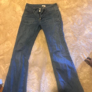 Blå bootcut jeans med knappar - Säljer ett par klassiska blå bootcut jeans med knappar framtill och fickor både fram och bak. Jeansen har låg midja och är perfekta för dig som gillar en tidlös stil med lite utsvängda ben.