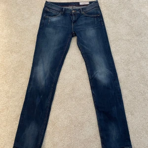 Blåa jeans från Replay - Snygga blå jeansbyxor från Replay med klassisk femficksdesign och extra dragkedjedetalj på fickan. Byxorna har raka ben och subtila slitningar för en cool look. Jenssen är ganska lågmidjade och har fina detaljer på bakfickorna. Jag har köpt dessa secondhand på Sellpy. Storleken på Jensen är oklar men jag tror att det är storlek 42.