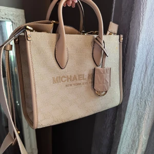  Michael Kors ”Mirella” Small Metallic Logo Jacquard Crossbody Bag - En äkta Michael Kors väska i modellen Mirella, använd ett fåtal gånger. Jättefin ljusbeige/ljusrosa färg med guld glittrig tråd i MK monogrammet. ✨🩷 Finns bild på insydd lapp i väskan som bevisar äktheten. Väskans identitet.  Style #35F2G7ZC5I