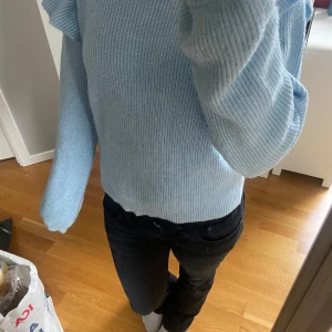 Ljusblå stickad tröja med volang från Vila - Säljer en ljusblå stickad tröja från Vila med långa ärmar och volangdetaljer vid axlarna. Tröjan har en rund halsringning och är ribbstickad för en snygg och bekväm passform. Perfekt för att addera lite färg till garderoben!