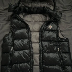 Moncler Väst M/L - Hej säljer en fin svart moncler väst i storlek 5 (IT),  som motsvarar M/L i Sverige. Västen är knappt använd, kan även mötas i stockholm! Skriv om du har fler frågor, priset är ej heller hugget i sten!