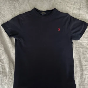 Marinblå Ralph Lauren t-shirt - Hej! Jag säljer denna snygga och stilrena bomulls T-shirten från Ralph Lauren! Den är i den klassiska ”Ralph Lauren marinblåa” färgen och är i S i barnstorlek vilket motsvarar cirka 140-150cm i längd. Skick 7.5/10 använd men väl omhändertagen och har bara få tecken på användning som inte påverkar helhetsintrycket vid användning!Äkta ✅. Hör av dig om du har några frågor och sånt! 😊