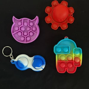 Färgglada pop it-väskor och nyckelring - Fyra små pop it-accessoarer i olika former och färger. En lila katt, en röd blomma, en blåvit nyckelring och en regnbågsfärgad figur. Perfekt som accessoar eller leksak att ha med sig.