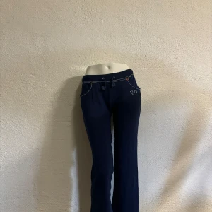 Mjukisbyxor - Mörkblå mjukisbyxor från True Religion med vita kontrastsömmar och snörning i midjan. Byxorna har bootcut-modell och broderad logga på fickan.  Står storlek L men passar mer som en S.