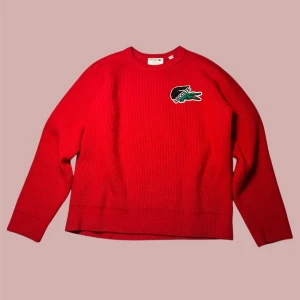 Röd stickad tröja från Lacoste - Säljer denna unika Lacoste tröjan då den blivit för liten. Tyvärr har den blivit lite nopprig men annars har den inga skador