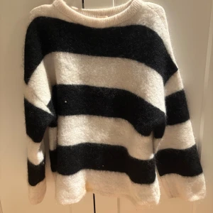 Randig stickad tröja - Säljer en mysig stickad tröja med breda svarta och vita ränder. Tröjan har en avslappnad passform och långa ärmar. Tröjan har en fläck längst nere som jag har tvättat men svår att få brot🥰