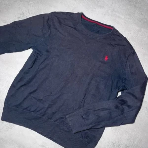 Mörkblå tröja från Ralph Lauren - Säljer en stilren mörkblå tröja från Ralph Lauren med det klassiska röda logotypbroderiet på bröstet. Tröjan har långa ärmar och ribbade muddar vid ärmslut och nederkant. Perfekt för en avslappnad och snygg look.