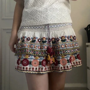 Vit kjol med broderade detaljer - Charmig vit kjol med färgglada broderier och tofsar. Den är från Zara.