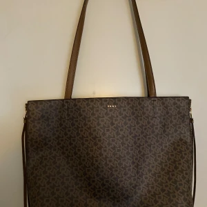Brun mönstrad axelväska från DKNY - Snygg brun axelväska från DKNY, nästan helt oanvänd, väskan är revesersibel och kan flippas in och ut, alltså 2 väskor i 1. Jättebra skick, pris kan diskuteras vid snabb affär💖🫶🏽