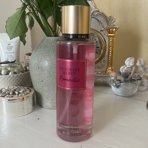 Victoria's Secret Romantic Fragrance Mist - Säljer en Victoria's Secret Romantic Fragrance Mist med en doft av rosa blomblad och mjuk mysk. Flaskan är genomskinlig med rosa vätska och har en elegant guldlock. Perfekt för en romantisk touch i vardagen.
