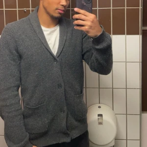 Cardigan kofta - Säljer en grå cardigan med knappar och sjalkrage. Perfekt för kyligare dagar med sin mjuka och bekväma passform. Koftan var storlek M men krymptes lite så nu passar den S och M. Skick 9/10 knappt använd.