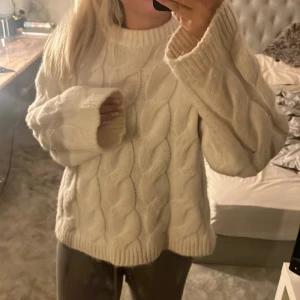 Vit stickad tröja med flätmönster - Mysig vit stickad tröja med ett klassiskt flätmönster. Perfekt för kyliga dagar med sin varma och bekväma design. Tröjan har långa ärmar och en rund halsringning.