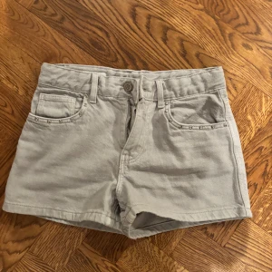 Grå shorts från Zara - Snygga Grå shorts från Zara med hög midja och dekorativa nitar vid fickorna. Perfekta för sommardagar och enkla att matcha med olika toppar. De har en klassisk femficksdesign och stängs med dragkedja och knapp.