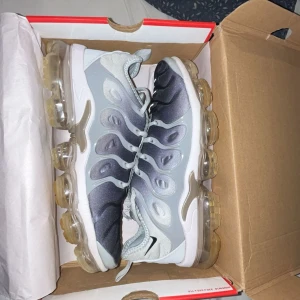 Nike Air vapormax plus wolf grey  - Snygga Nike Vapormax sneakers i grå och svart med transparent sula. Skorna har en modern design med snörning och är perfekta för en sportig look. Skorna är i bra skick använda ett par gånger men det har tagit hand om dem. Finns bara 1 litet problem med skorna. Det är att dem har ett jättelitet hål längs fram på skon som ni kan se på bindarna. Annars är dem helt okej. Priset kan diskuteras och självklart är skorna äkta!