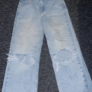 Ljusa jeans med slitningar från GinaTricot - Säljer ett par ljusa jeans från ginaTricot med coola slitningar på knäna. De har en klassisk femficksdesign och en bekväm passform. Perfekta för en avslappnad stil.