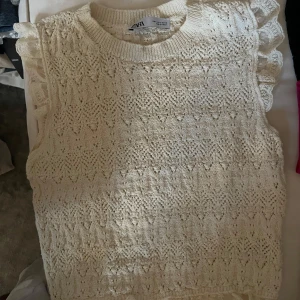 Vit stickad topp från Zara - Säljer en söt vit stickad topp från Zara med volangdetaljer vid ärmhålen. Toppen har ett fint mönster och är perfekt, Passar bra till både jeans och kjol.