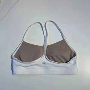 Vit sport-bh från Lululemon - Säljer en vit sport-bh från Lululemon med smala axelband och en enkel design. Perfekt för träning och ger bra stöd. Materialet är mjukt och bekvämt.