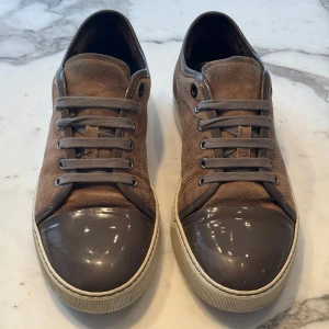 Bruna sneakers med grå detaljer - Snygga bruna Lanvins med grå snörning och med toecap. Skorna har en stilren design med en kombination av mocka och glansigt material på tån. Perfekta för en avslappnad stil.