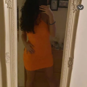 Orange klänning från Gina Tricot - Säljer en snygg orange klänning från Gina Tricot. Klänningen har en unik textur med vågiga detaljer och är ärmlös. Perfekt för att sticka ut med sin starka färg och stilrena design. Passar perfekt för sommarens alla tillfällen! Aldrig använt ! Storleken är i L men den passar perfekt om man är i S-M