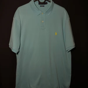 Ralph Lauren piké | Turkos| Custom Fit | Stl L - Läs nedan för mer info!😊  Säljer en stilren ljusblå pikétröja från Ralph Lauren med klassisk krage och knappslå. Tröjan har en broderad gul logotyp på bröstet och är i en bekväm passform. Perfekt för en avslappnad men snygg look.  Produktinformation:  ✅ Märke: Ralph Lauren  ✅ Storlek: L ✅ Färg: Turkos ✅ Material: Bomull ✅ Passform: Custom fit – perfekt att styla med jeans eller chinos ✅ Skick: Mycket bra skick, knappt använd  Frakt och betalning: 📦 Snabb leverans – skickar inom 1-2 dagar efter 📦