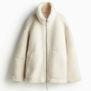 Vit teddyjacka med dragkedja - Mysig vit teddyjacka med dragkedja framtill och stora fickor. Perfekt för kyliga dagar med sin fluffiga och varma design. Jackan har en avslappnad passform och långa ärmar.