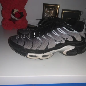 Nike Air Max Plus i svart och grått - Säljer ett par Nike Air Max Plus med ett coolt mönster i svart och grått. Skorna har den klassiska Tn-loggan på hälen och snörning framtill. Perfekta för dig som vill ha en stilren och sportig look. Bra skick och bra pris för hur mycket den kostar nypris