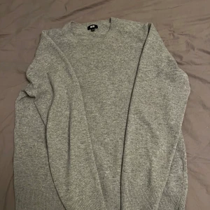Grå stickad tröja från Uniqlo - Säljer en stilren grå stickad tröja från Uniqlo. Perfekt för kyligare dagar med sin mjuka och bekväma passform. Tröjan har långa ärmar och ribbade kanter vid ärmslut och nederkant. Passar utmärkt till både jeans och chinos.