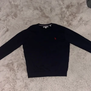 Svart/mörkblå tröja från La Polo Assn - Snygg svart/mörkblå tröja från La Polo Assn med ett rött broderat emblem på bröstet. Tröjan har långa ärmar och en klassisk rund halsringning. Perfekt för en stilren look. Tröjan är använd tre gånger och är perfekt passform i storlek S och är riktigt skön och varm.