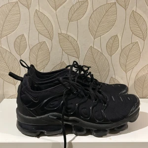 Svarta Vm Nike sneakers - Säljer ett par svarta Nike sneakers med snörning och en unik sula. Skorna har en modern design med diskreta detaljer och är perfekta för en sportig look. De är bekväma och stilrena, idealiska för vardagsbruk.