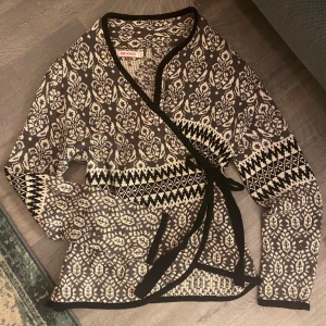 Mönstrad omlottkofta från Indiska likt od molly - Säljer en snygg mönstrad omlottkofta från Indiska i svart och beige. Koftan har långa ärmar och ett knytband i midjan. bra skick 
