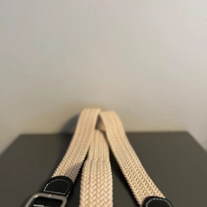 Beige flätat bälte med svart spänne - Snyggt beige flätat bälte med ett stilrent svart spänne. Perfekt för att ge en extra touch till din outfit. Bältet har en klassisk design som passar till många olika stilar.