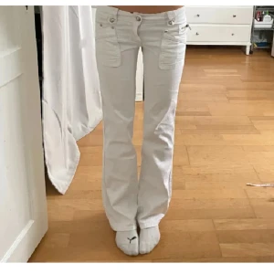 Vita lågmidjade byxor med fickdetaljer - Snygga vita byxor med låg midja och unika fickdetaljer fram och bak. Byxorna har en bootcut-stil och är perfekta för en trendig look. De har knappar och dragkedja framtill.