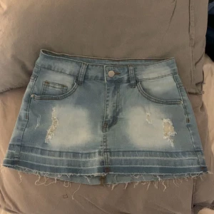 Jeanskjol i ljusblå denim - Trendig kort jeanskjol i ljusblå denim med slitna detaljer och rå kant. Perfekt för en avslappnad stil. Osäker vart den är köpt 