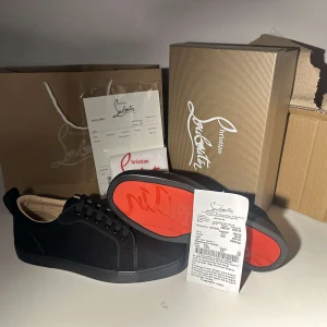 Svarta sneakers från Christian Louboutin - Snygga svarta sneakers från Christian Louboutin med den ikoniska röda sulan. Skorna har en stilren design med snörning och är tillverkade i ett elegant material som ger en lyxig känsla.