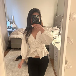 Vit omlottopp från Boohoo - Säljer en stilren vit omlottopp från Boohoo med trekvartsärmar och knytband i midjan. Toppen har en v-ringad design och volangdetaljer som ger en feminin touch. Perfekt för att klä upp eller ner beroende på tillfälle. Pris kan diskuteras, passa folk i xs 💞