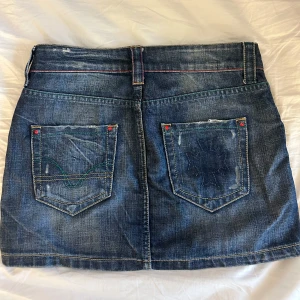 Jeanskjol från Casucci - Snygg jeanskjol från Casucci i blå denim. Kjolen har en kort längd och dekorativa röda nitar. Jag köpte den i Italien och är nu för liten för mig! 