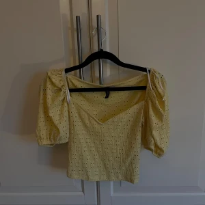 Gul blus med puffärmar - Säljer en söt gul blus med puffiga trekvartsärmar och ett v-ringad snitt. Blusen har ett diskret hålmönster som ger en romantisk touch. Perfekt för vår och sommar!