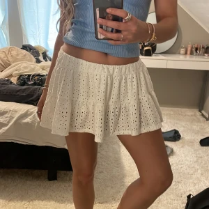 Vit kortkjol med broderade detaljer - Säljer en söt vit kortkjol med broderade detaljer. Kjolen har en luftig passform och är perfekt för varma dagar. Den är elastisk i midjan för extra komfort. Passar bra till en avslappnad sommarlook.