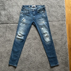 Blå jeans från Replay - Snygga blå jeans från Replay med slitna detaljer och en modern look. De har en klassisk femficksdesign och är tillverkade i hållbar bomull. Perfekta för en avslappnad stil. Storlek 30 waist och 32 length, 