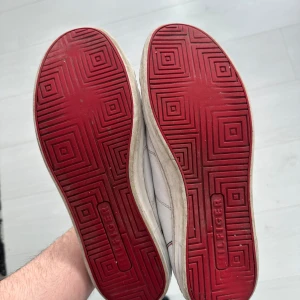 Vita sneakers från Tommy Hilfiger - Snygga vita sneakers från Tommy Hilfiger med röd och blå detalj på sidan. Skorna har snörning och en röd sula med mönster. Perfekta för en stilren look. Förslag på pris tas imot ochså ! 