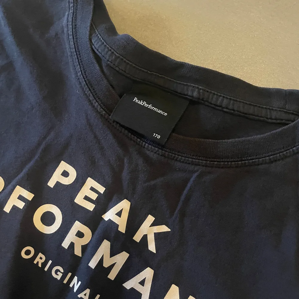 Säljer en svart t-shirt från Peak Performance med tryck på framsidan. T-shirten har en klassisk rund hals och korta ärmar. Perfekt för en avslappnad stil.. T-paidat.