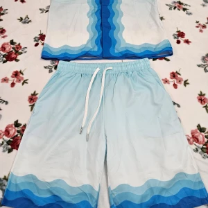 Blå och vita shorts från Casablanca Storlek - Snygg blå och vita sett från Casablanca med vågigt mönster. Shortsen har en bekväm passform med snörning i midjan. Skjortan har en ficka på vänstra bröstet och detailjer på ryggen. Perfekta för sommarens äventyr! 🌊🏖☀️🌴