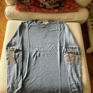 Blå långärmad tröja från Springfield - Säljer en stilren blå långärmad tröja från Springfield med snygga armbågslappar i kontrasterande färg. Perfekt för en avslappnad look. Tillverkad i mjuk bomullsmix för extra komfort.