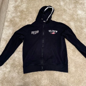 Svart hoodie Polo Club -  Mörkblå hoodie med dragkedja från Polo Club Saint Vincent och U.S. Crew. Hoodien har texttryck på bröstet och en ficka på magen.  Skick: 8/10. Varan har inga eller små tecken på användning. Färgen har blivit lite ljus enbart Storlek: S/M Färg: grå Ord. Pris: 329  Din stil: spara inlägget så du inte missar denna kappa Inte din stil: Kolla min profil. Du kommer hitta något för alla kön och åldrar.