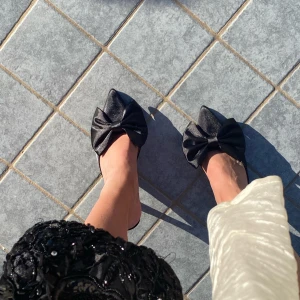 Svarta klackar med rosett - Eleganta svarta pumps i satin med en stor dekorativ rosett på ovansidan. Skorna har en spetsig tå och en smal klack, vilket ger en stilren och sofistikerad look. Köpta utomlands. Använda ett fåtal gånger. Klackhöjd kanske 8? Sköna att gå i. 